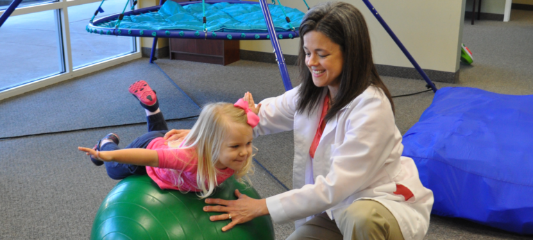 therapist working with a small girl using a therapy ball
