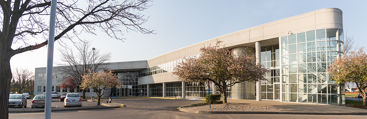 the front of the building with trees in bloom and a view of the parking lot